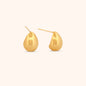 Close-up of gold teardrop earrings, showcasing their smooth, polished surface and modern, sculptural design.
