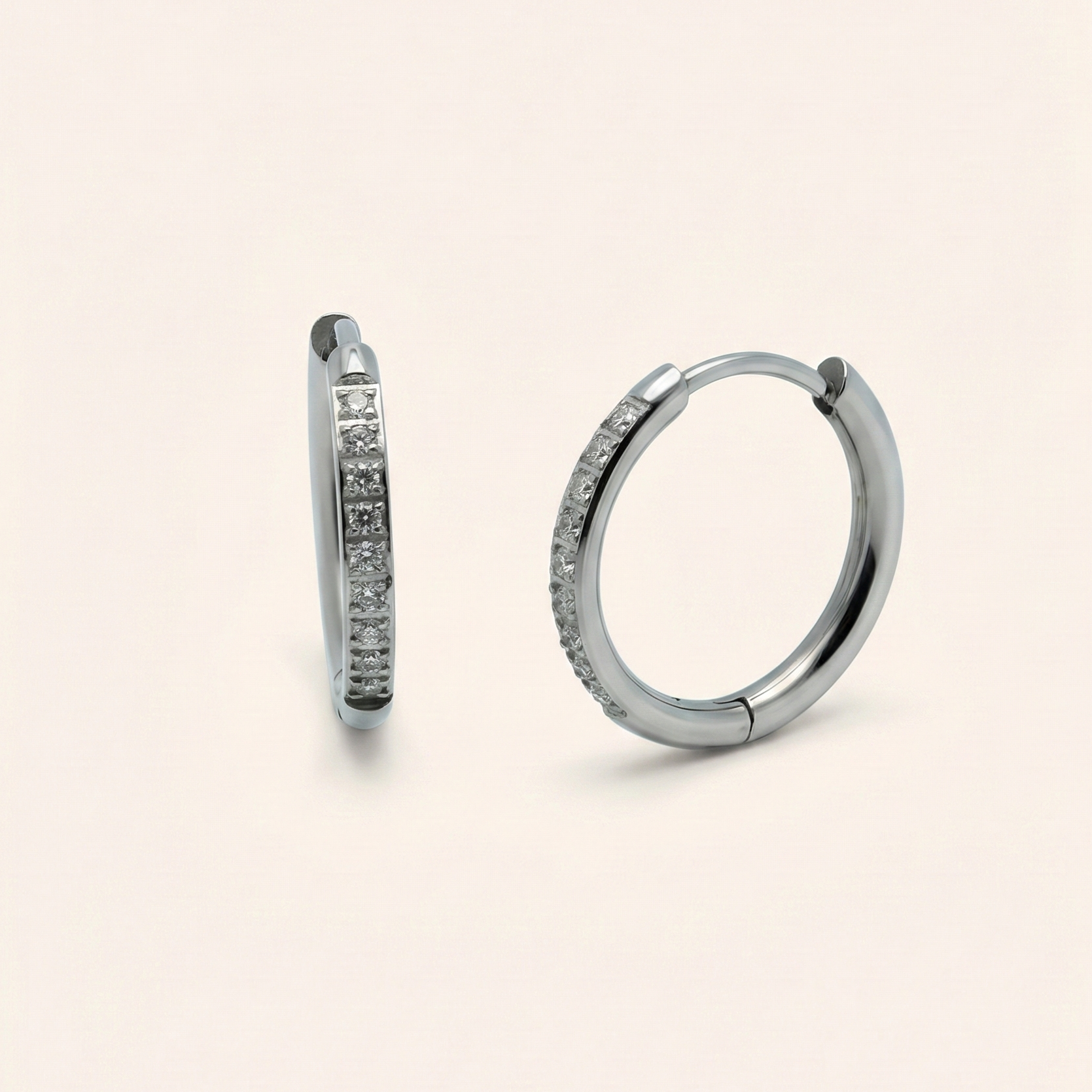 Pair of silver hoop earrings with embedded stones on a beige background