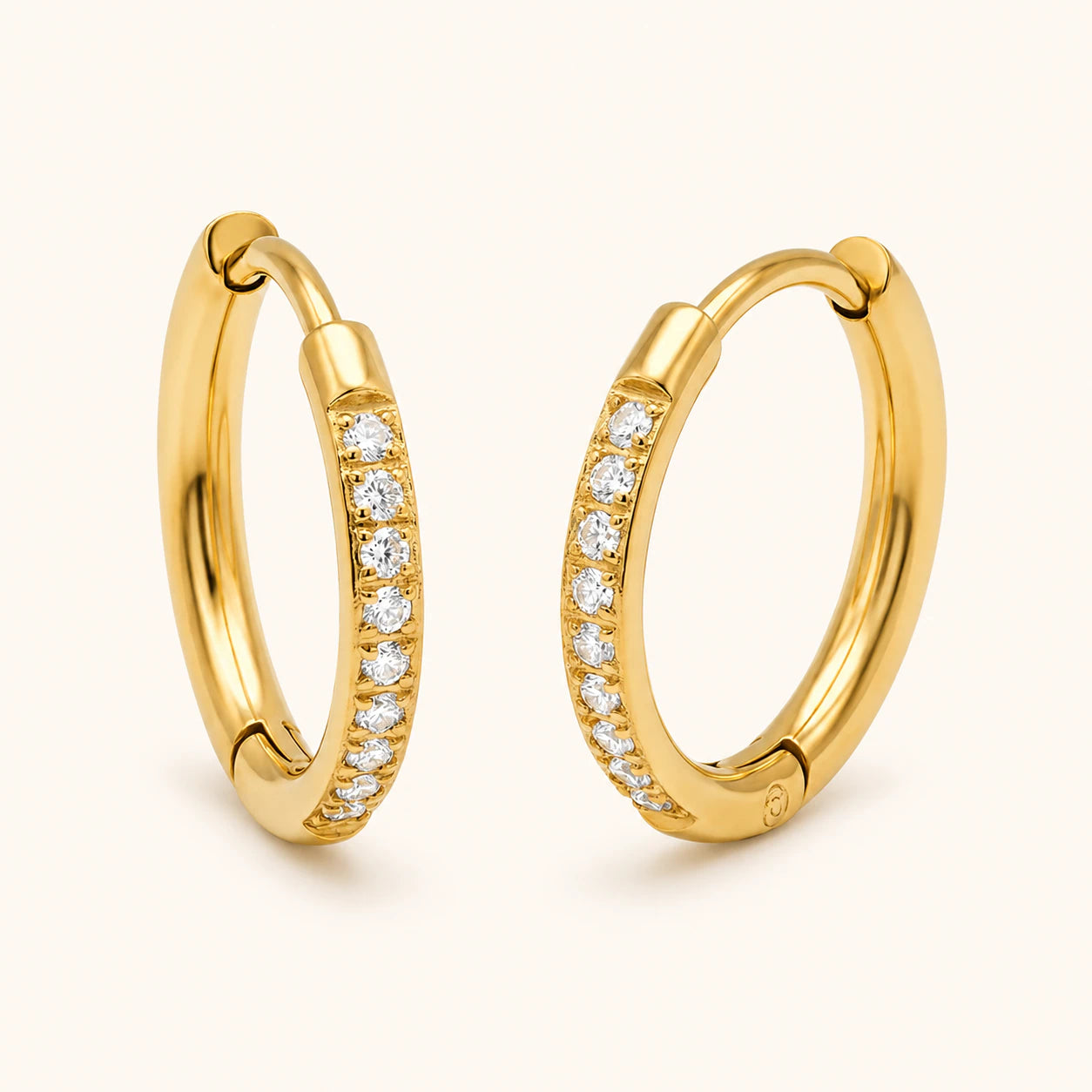Gold hoop earrings with embedded diamonds on a light beige background