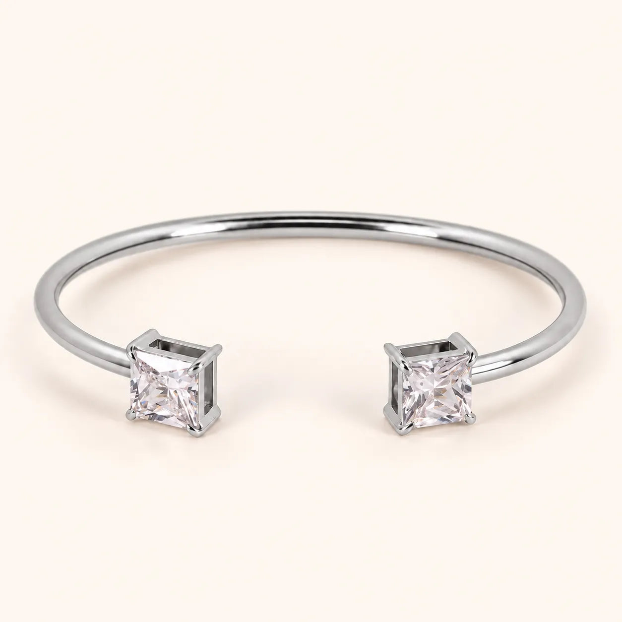 A silver-toned open cuff bangle bracelet with two princess-cut clear gemstones, shown on a light cream background.