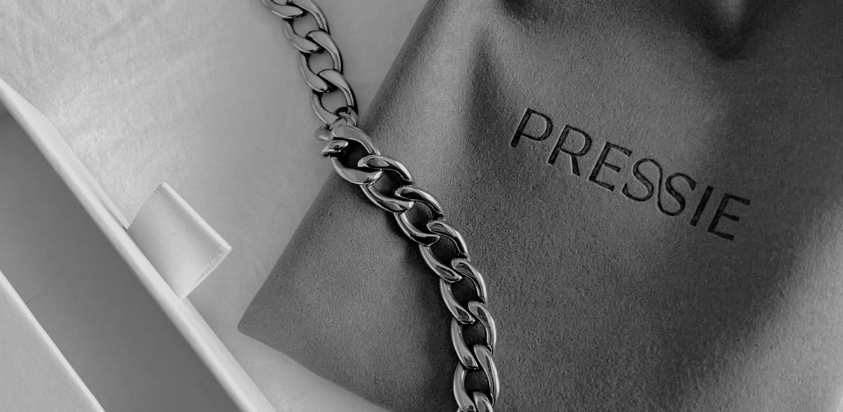 Black-and-white close-up of a chain necklace on PRESSIE branded gift packaging