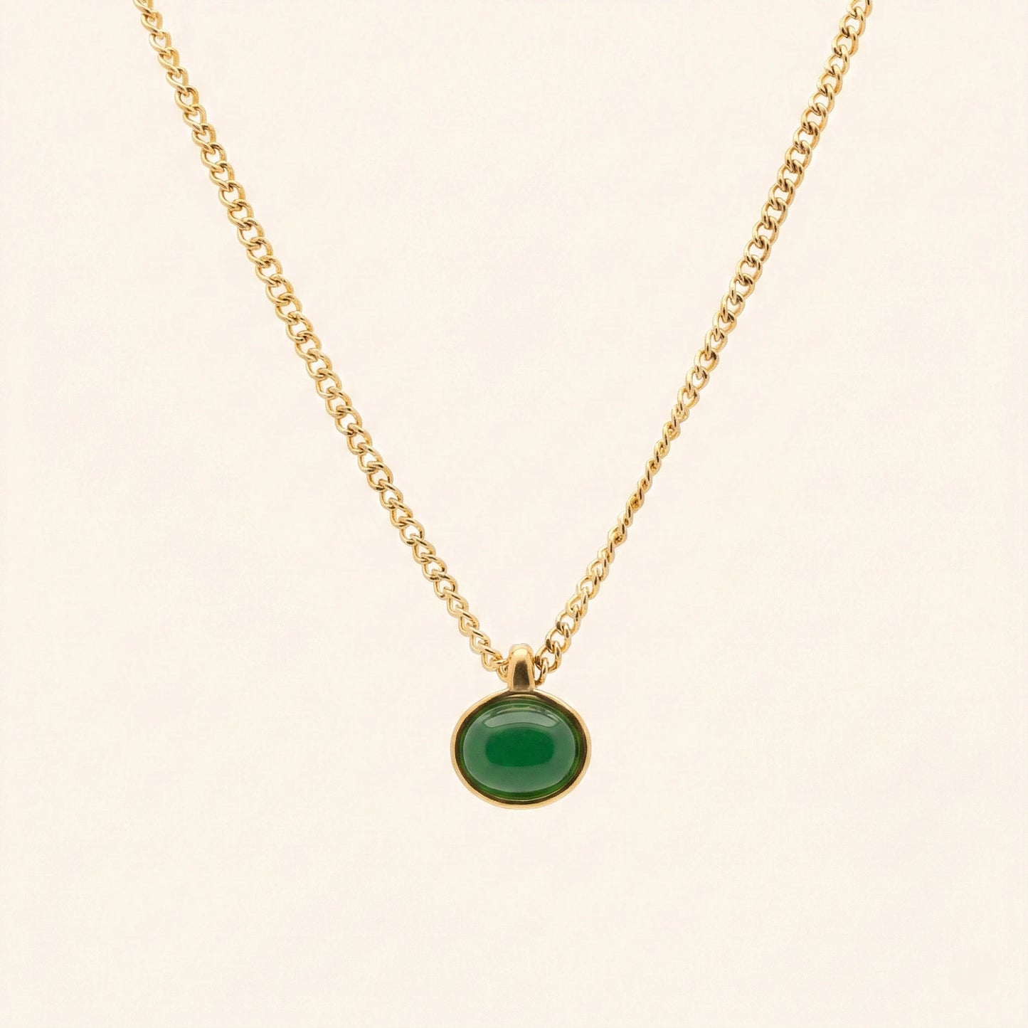 Gold necklace with a green pendant on a beige background