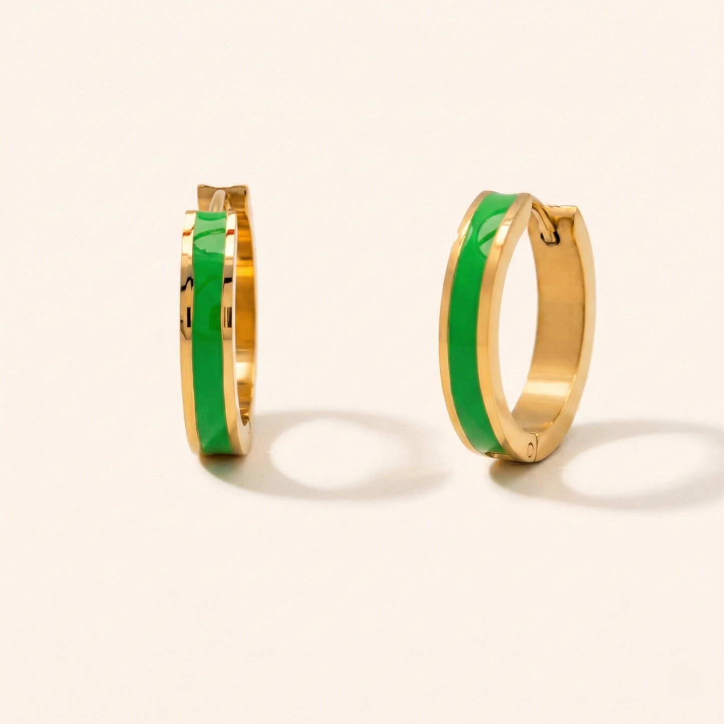 Gold hoop earrings with green interior on a light beige background